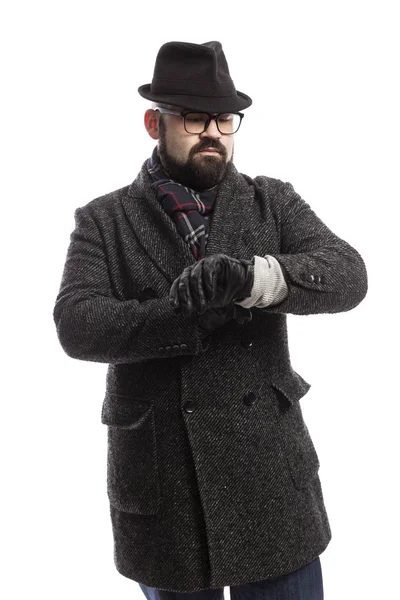 Un hombre elegante con barba en abrigo y sombrero mira su reloj. Fondo blanco . — Foto de Stock