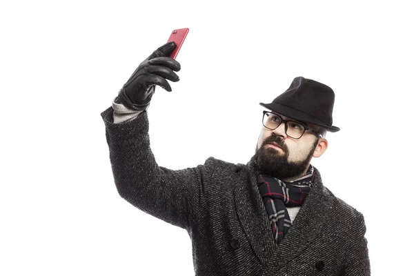 Eleganter Mann mit Bart, stylischem Mantel und Hut macht Selfie. isoliert über weißem Hintergrund. — Stockfoto