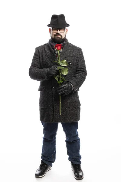 Eleganter Mann mit Bart, in stylischem Mantel und Hut mit roter Rose in der Hand. volle Höhe. isoliert über weißem Hintergrund. — Stockfoto