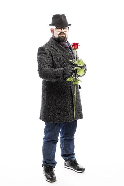 Eleganter Mann mit Bart, in stylischem Mantel und Hut mit roter Rose in der Hand. volle Höhe. isoliert über weißem Hintergrund. — Stockfoto