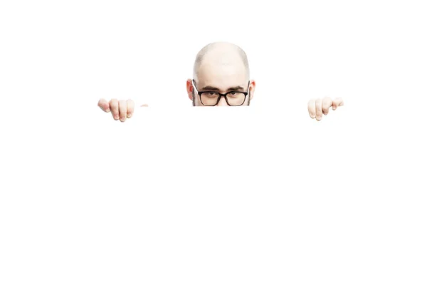 A bald man with glasses peeks out from behind an empty banner. Isolated over white background — Stock Photo, Image