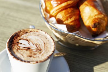 Kapuçino ve taze kruvasanlar güneşli bir günde bir sokak kafesinde bir masada. Yakın plan..