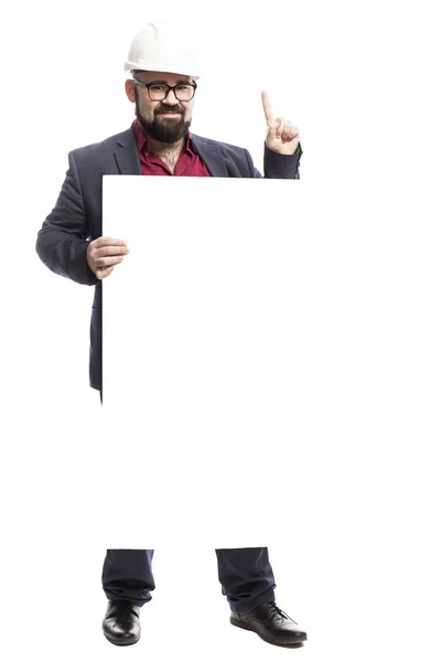 A man in glasses with a beard in a white construction helmet holds an empty banner. Dressed in a formal suit. Isolated on a white background. — Stock Photo, Image