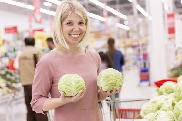 Jovem mulher loira sorridente com cabeças de repolho em um supermercado. Vegetarianismo e dieta alimentar crua . — Fotografia de Stock