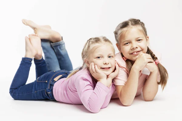 Dwie małe dziewczynki leżą w pobliżu i uśmiechają się. Białe tło. — Zdjęcie stockowe
