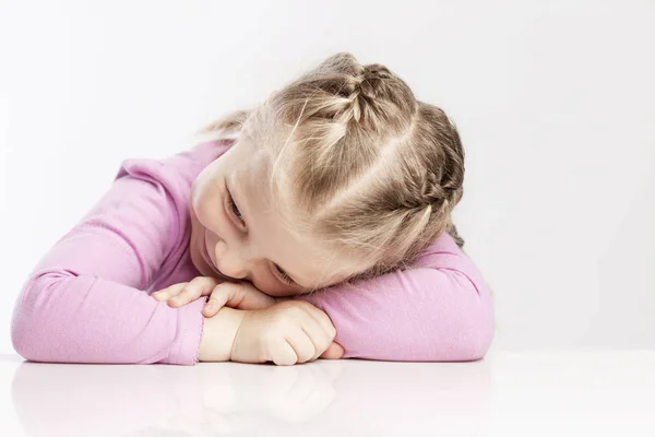 La bambina posò la testa sul tavolo. Sfondo bianco. Primo piano . — Foto Stock