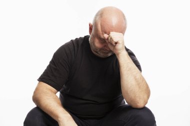 Siyah tişörtlü kel bir adam kafasını elinde tutarak kameraya bakıyor. Beyaz arkaplan.