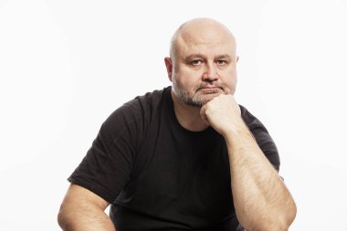 Siyah tişörtlü kel bir adam kafasını elinde tutarak kameraya bakıyor. Beyaz arkaplan.