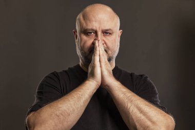 Kel adam ellerini yüzüyle dua etmek için katladı. İnanç ve umut. Koyu arkaplan.