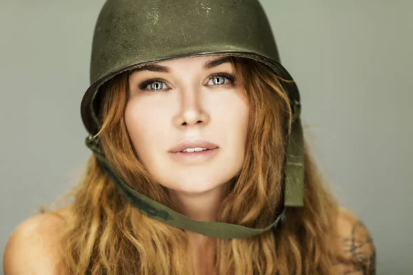 Beautiful young woman with long red hair in a military helmet. Close-up.