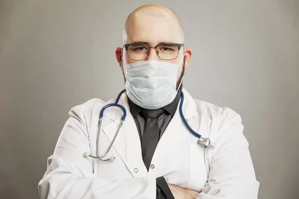 Een mannelijke dokter in een witte jas en een medisch masker. Grijze achtergrond. — Stockfoto