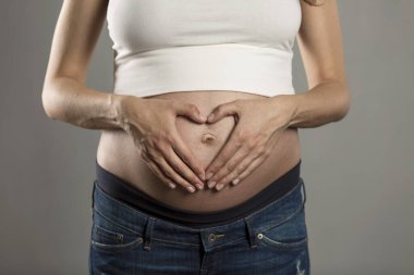 Gri arka planda hamile bir kadının koca göbeği. Yakın plan..