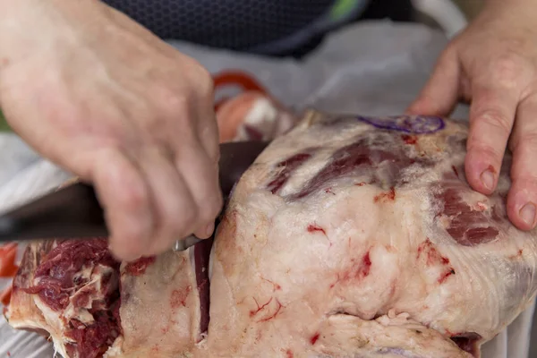 Hands with knives butcher the carcass of meat. Close-up.