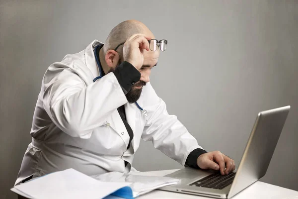 Mężczyzna Białym Płaszczu Zadziwia Się Komputerem Okularach Szare Tło Pandemia — Zdjęcie stockowe