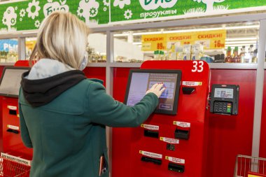 Moskova, Rusya, 03 / 26 / 2020: Sarışın bir kadın self-servis terminalindeki bir süpermarketten satın alımlar için ödeme yapıyor.