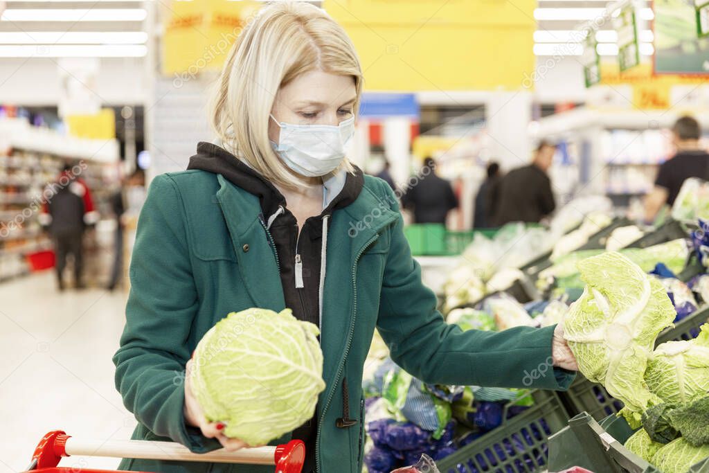 Woman blonde in a medical mask chooses vegetables in a supermarket. Self-isolation in a pandemic. 