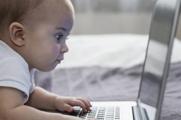 The baby looks with interest at the laptop screen. New generation. Close-up.