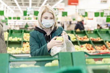 Tıbbi maskeli sarışın bir kadın süpermarketten alışveriş yapıyor. Koronavirüs salgınında karantina.