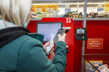 Moskova, Rusya, 03 / 26 / 2020: Sarışın bir kadın self-servis terminalindeki bir süpermarketten satın alımlar için ödeme yapıyor.