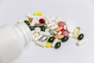 Çok renkli haplar beyaz bir şişeden masaya döküldü. Koronavirüs salgını sırasında karantina. İlaçlar. Yakın plan. Beyaz arka plan. Metin için boşluk.