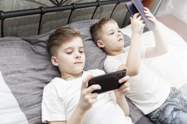 Üzgün erkek kardeşler ellerinde telefonlarla yatakta yatıyorlar. Koronavirüs salgını sırasında kendini izole etme. İşaret fişeği.