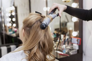 Sarışın bir kadın, profesyonel bir güzellik salonunda saç maşasına bir tutam saç yapıştırıyor. Yakın plan..