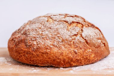 Masanın üzerinde un kaplı mayalanmış kahverengi bir ekmek. Beyaz bir arkaplanda. 