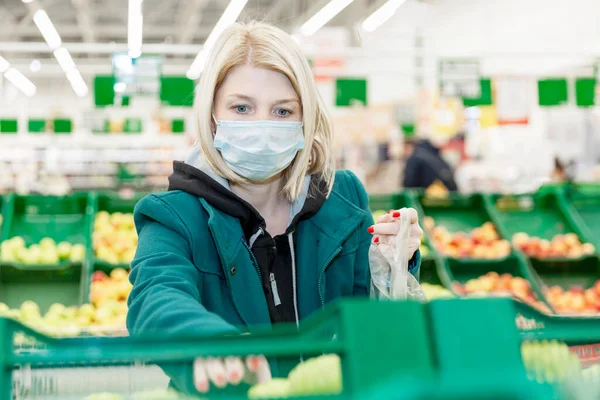 Woman with a mask on standing in an aisle at a supermarket picking fruit. The coronavirus outbreak forces people to stock up on fruits, vegetables and other foods and products.