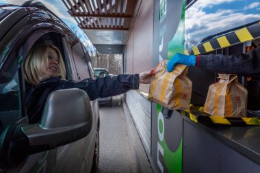 Moskova, Rusya, 26 / 04 / 2020: Arabadaki sürücü McDonald 's vitrininden sipariş alıyor. Koronavirüs salgınına karşı kendini izole etme döneminde popüler bir restoran. Çanta transferi..