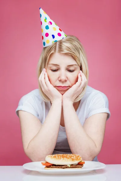 Uma Mulher Casa Roupas Gorro Festivo Senta Triste Frente Hambúrguer — Fotografia de Stock