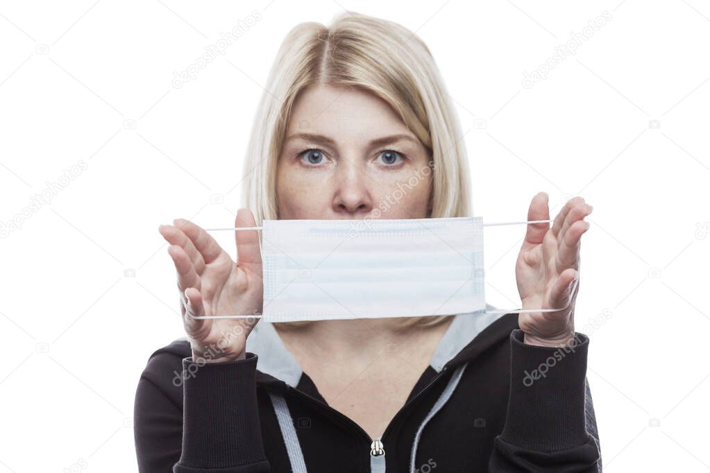 A blonde woman is holding a medical mask in front of her. Precautions during seasonal allergies. Self-isolation mode in the coronavirus pandemic. Close-up.Isolated on a white background. Blurred.