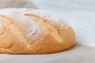 Hafif bir mutfak masasında çarşaf havlusunda el yapımı güzel bir ekmek. Sağlıklı beslenme. Yakın çekim. Yan görünüm.