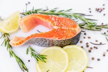 Biftek şeklinde dilimlenmemiş alabalık. Yanında limonlar ve baharatlarla. Odaklı önplan.