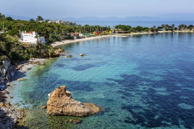 Turkuaz mavi denizde ve güneşli bir günde yeşil kıyıda kalp şeklinde büyük bir taş. Güzel körfezin manzarası harika. Rahatla ve sakinleş. Kartpostal Metin için boşluk.