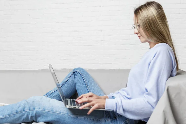 Young Girl Sits Gray Sofa White Brick Wall Laptop Her — Stock Photo, Image