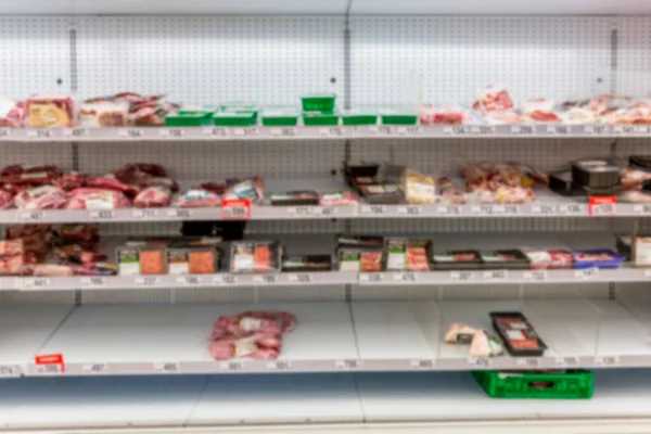 Half empty supermarket shelves with chilled smoked meat delicacies. Popular unhealthy foods. Front view. Blurred.