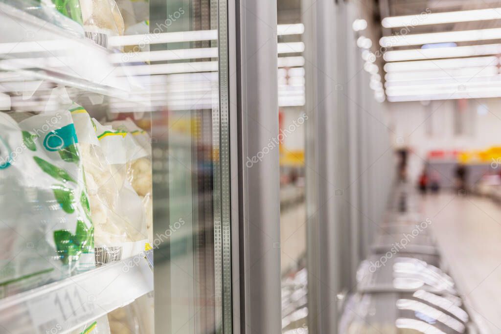 A row of display cases with frozen foods in a supermarket. Fresh vegetables and berries in packages. Vitamins and a healthy diet. Side view. Blurred.