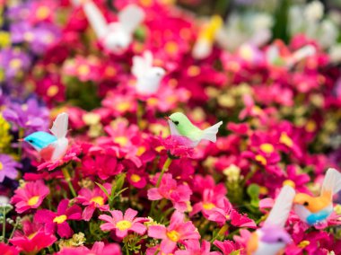 Kırmızı yapay çiçekler üzerinde yeşil sahte kuş