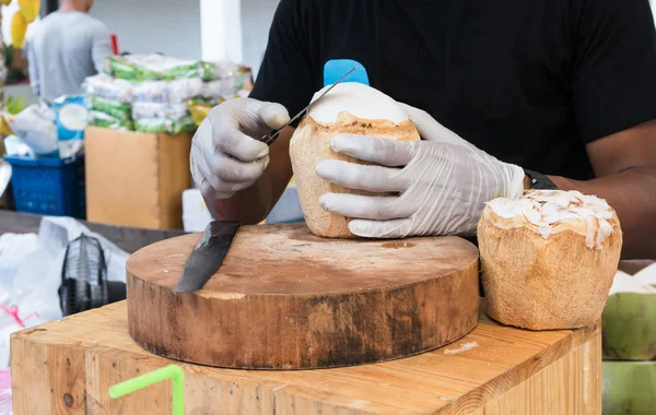 Mãos com luvas cortando a carne de coco com faca longa na madeira — Fotografia de Stock