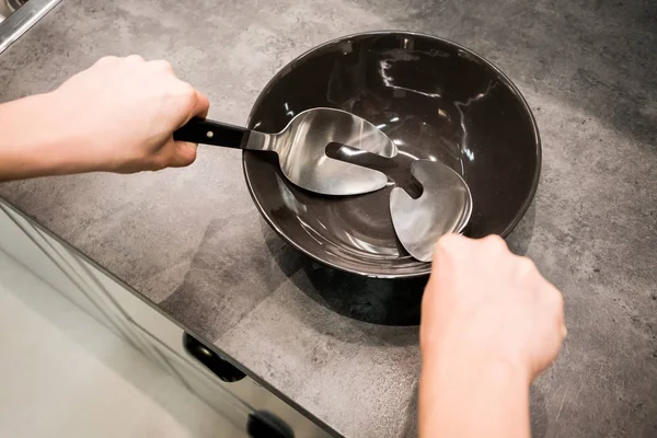 Manos de mujer sosteniendo cuchara de cocina y tenedor sobre porcelana negra — Foto de Stock