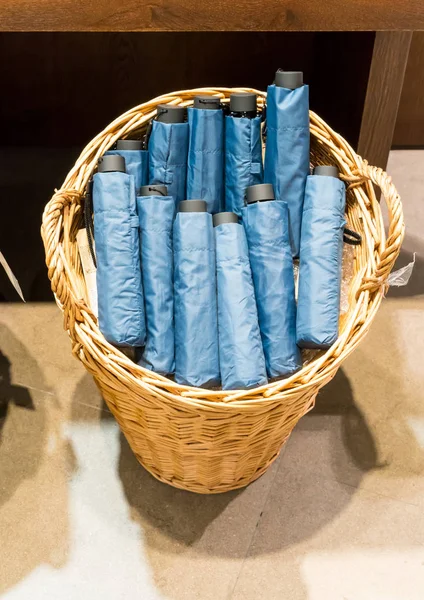Guarda-chuvas azuis dobráveis em cesta de vime no chão de cimento — Fotografia de Stock