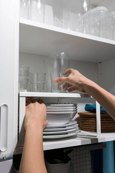 Mujer mano sosteniendo vidrio y cuencos en el estante de cabi de madera blanca — Foto de Stock