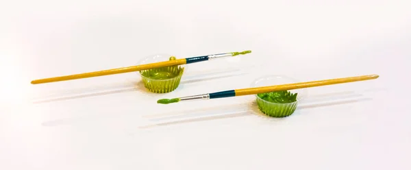 Färgglada penslar med grön färg i liten plastmugg und — Stockfoto