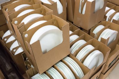 Stacks of white and round shaped porcelain plates in boxes. clipart
