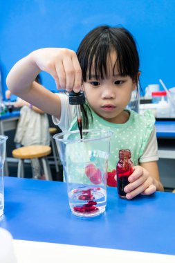 B bir bardağa kırmızı renk eklemek için damlacık kullanan anaokulu kız