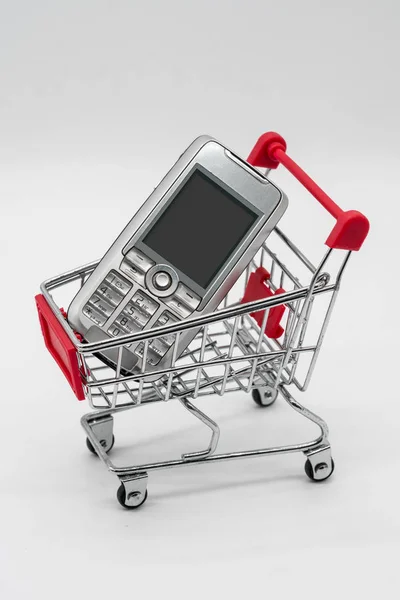 Telefone celular com carrinho de compras isolado em branco — Fotografia de Stock