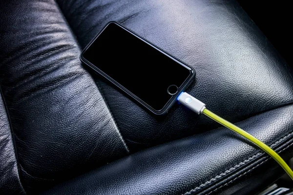 Black phone is charging by green cable inside car against black — Stock Photo, Image