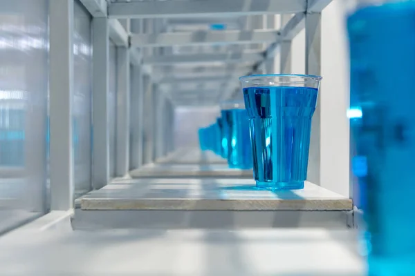 Água azul dentro copo de plástico transparente na prateleira de metal branco structu — Fotografia de Stock