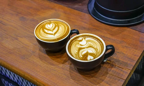 Filiżanek kawy z pięknym Latte art na stół z drewna. — Zdjęcie stockowe