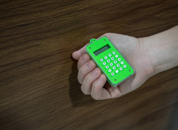 Mão segurando pequena calculadora digital verde contra backg de madeira — Fotografia de Stock